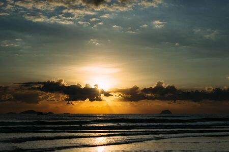 Sea, sunrise, clouds letting in the sun's rays reflection of the sun on the shore, blue skyの写真素材