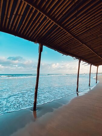 Seascape, sea view from under the bamboo roof. Waves at sea, sea tide, sandy shore. Beautiful clouds in the sky. Traveling in Asia. Bamboo buildings on the beach.の写真素材