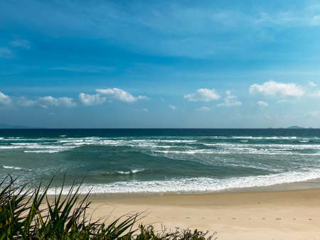 Sandy seashore, calm soft waves at sea, sunny weather, blue sky with white clouds. Empty long beach with a beautiful sea view. White foam from a sea waveの写真素材