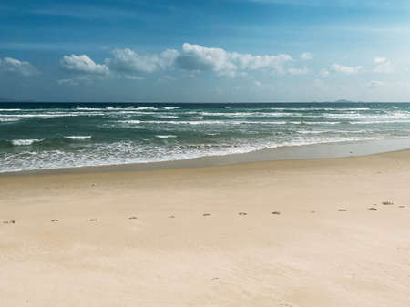 Sandy seashore, calm soft waves at sea, sunny weather, blue sky with white clouds. Empty long beach with a beautiful sea view. White foam from a sea waveの写真素材