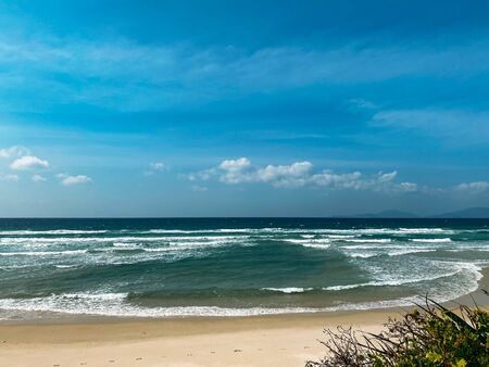 Sandy seashore, calm soft waves at sea, sunny weather, blue sky with white clouds. Empty long beach with a beautiful sea view. White foam from a sea waveの写真素材