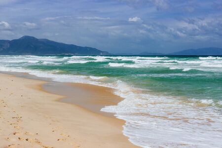 Sandy seashore, calm soft waves at sea, sunny weather, blue sky with white clouds. Empty long beach with a beautiful sea view. White foam from a sea waveの写真素材