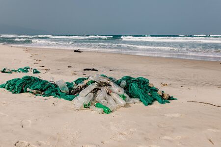 Plastic bottles and other rubbish thrown on the sandy seashore, trash on the sea beach. ecological problem. Environmental pollution. Dirty sandy beach. Old fishing net thrown to the seashore,の写真素材