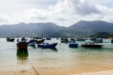 View of the island, sandy beach, clear blue sea. Traditional Asian fishing boats stand in a welcoming bay. White clouds on a blue sky. Travel in Vietnamの写真素材