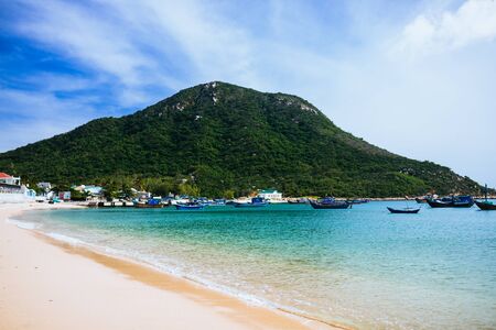 View of the island, sandy beach, clear blue sea. Traditional Asian fishing boats stand in a welcoming bay. White clouds on a blue sky. Travel in Vietnamの写真素材