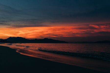 Beautiful sunrise, sunset of the sun through the clouds, the rays of the sun through the clouds, sandy seashore with small waves, warm morning light in a tropical area near the sea.の写真素材