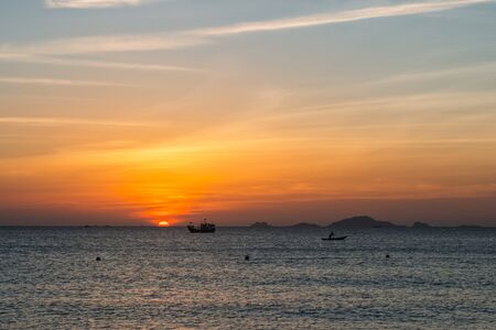 Colorful dawn, sunset on a calm sea, sunrise. Silhouette of a fishing boat on the horizon against the background of the sun. Beautiful sea background, landscape. Island on the horizon. Fiery colors.の写真素材