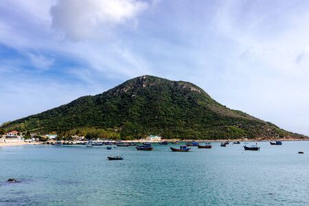 View of the island, sandy beach, clear blue sea. Traditional Asian fishing boats stand in a welcoming bay. White clouds on a blue sky. Travel in Vietnamの写真素材