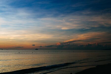 Beautiful sunrise, sunset of the sun through the clouds, the rays of the sun through the clouds, sandy seashore with small waves, warm morning light in a tropical area near the sea.の写真素材