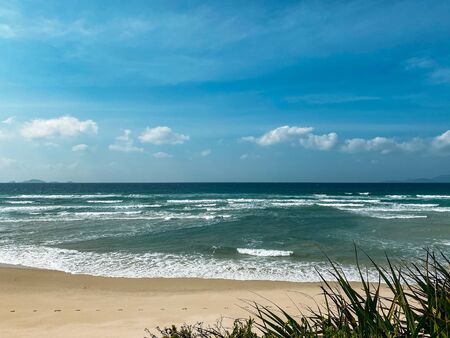 Sandy seashore, calm soft waves at sea, sunny weather, blue sky with white clouds. Empty long beach with a beautiful sea view. White foam from a sea waveの写真素材