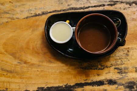 A cup of hot espresso in a dark cup on a black saucer with milk separately. Aromatic coffee stands on an old wooden brown table. Copy place. A good start to the dayの写真素材