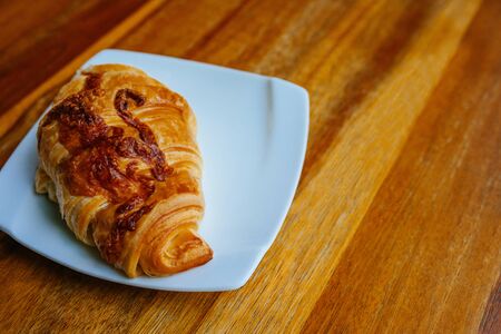 Tasty fresh croissant on a white saucer. Cheese croissant on an empty wooden brown table, light breakfast, lunchの写真素材