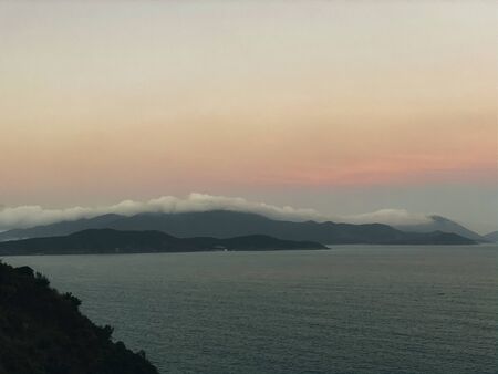 Sunset on the sea with a panoramic view from the top of the cliff. View of the rocky sea shore, waves on the shore. Mountains on the horizon. Beautiful sky color from the setting sun. Beautiful dramatic seascapeの写真素材