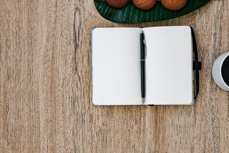 Flat lay, open blank U-turn of a notepad with white paper, morning recording of plans, breakfast with aromatic coffee and chocolate chip cookies. Composition on a light wooden background, place for text and insert. Copy place.の写真素材