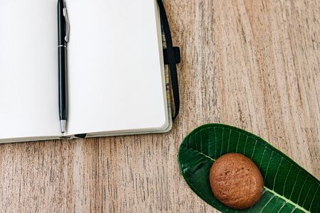 Notepad with white paper, unfolded, lies on a wooden background, a pen on the back of a notebook. chocolate cookies for breakfast. top view, flat lay, open for writing, place for text, copy space. Plans for the day.の写真素材