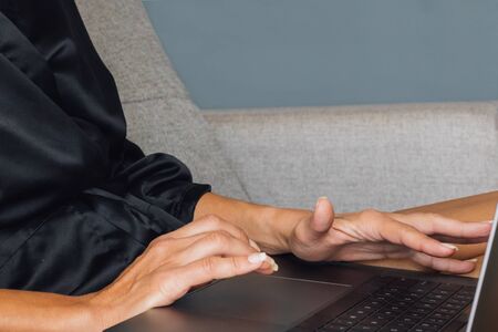 A woman with a mask on her face works on a laptop on the couch, quarantine time, self-isolation, work at home. Morning after waking up, coffee with cookies in the morning, flowers on the tableの写真素材