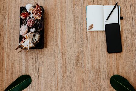 Flat lay, top view of a notepad with white paper and pen for planning an upcoming trip, or freelancer plan. Smartphone to view the route. Seashells on a notebook and tropical sheets nearby. Travel concept. Place for text or image, copy placeの写真素材
