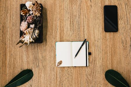Flat lay, top view of a notepad with white paper and pen for planning an upcoming trip, or freelancer plan. Smartphone to view the route. Seashells on a notebook and tropical sheets nearby. Travel concept. Place for text or image, copy placeの写真素材