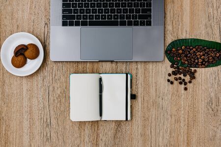 Flat lay of the workplace. Freelance work laptop smartphone and note pad. Morning coffee with cookies. Copy space on wooden background and notepad. Top view, a notebook next to a laptop, a pen for recording cases. Place for textの写真素材