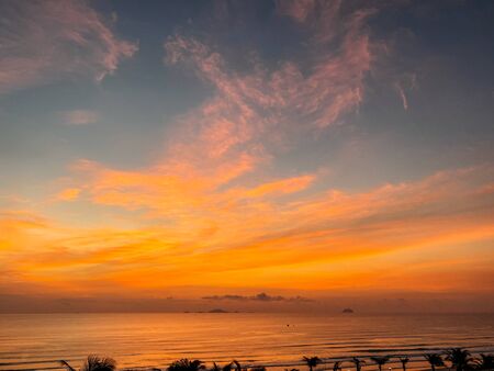 Dawn on the sea with a view of the horizon, colorful sky from the sun rays, clouds on a blue sky. Sandy beach on the seashore, waves on the sea, copy placeの写真素材