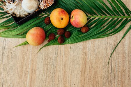 Flat lay Mix of Exotic fruits and palm leaf on a brown background: mangoes, lychee.  set for a...