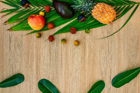 Flat lay Mix of Exotic fruits and palm leaf on a brown background: pineapples, Avocado, mangoes, mangosteen, lychee, citrus fruits. A great set for a healthy diet. Vegetarianism with fruits. Copy space, wood backgroundの写真素材