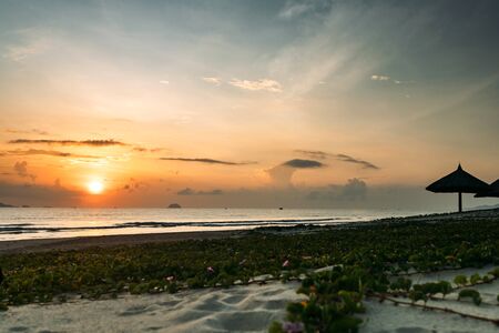 Beautiful sunrise, sunset of the sun through the clouds, the rays of the sun through the clouds, sandy seashore with small waves, warm morning light in a tropical area near the sea.の写真素材