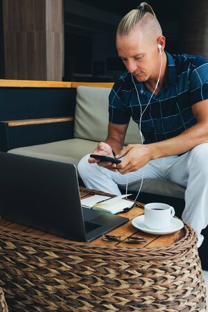 A male freelancer, a young businessman, doing remote work while sitting in a cafe with a cup of...