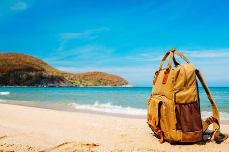 Tourist stylish brown backpack on the shore of a tropical beach during travel, vacation. Sandy beach, sea and mountain views in the background. Freelancer backpack. Copy placeの写真素材