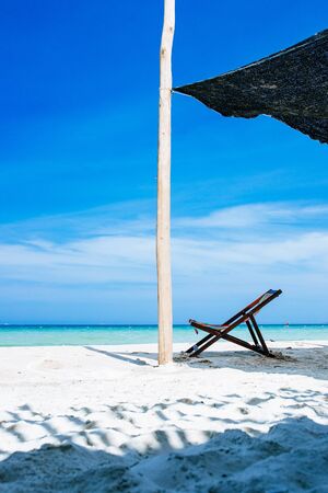 One deck chair is in the shade on the ocean, without people. With a blue sky with white clouds on the background. A place of relaxation and rest on the beach.の写真素材