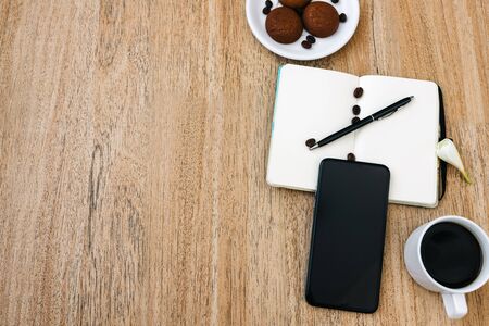 Flat lay composition with notepad, smartphone, cup of coffee and breakfast cookies. Record a plan for the day. Morning workplace. Pen on an open writing pad, for writing. Copy space, space for textの写真素材