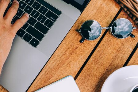 Hands of a man working at a laptop top view of a workspace, on a wooden table with a cup of coffee and a notebook for. business concept. Remote work. Copy space, wood backgroundの写真素材