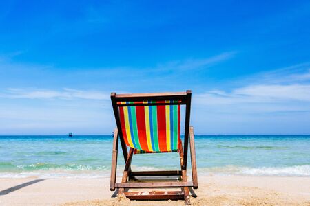 One deck chair on a sandy tropical beach with clear sea, bruise color of water and blue sky on the background.の写真素材