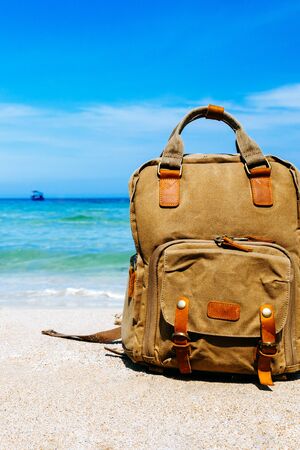 Tourist stylish brown backpack on the shore of a tropical beach during travel, vacation. Sandy beach, sea views in the background. Freelancer backpack. Copy placeの写真素材