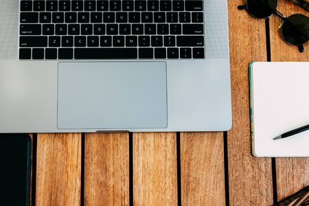 Flat lay of workspace for working at a laptop,  a brown wooden table with a cup of coffee and a notebook for recording cases. Freelance concept. Remote work. Copy placeの写真素材