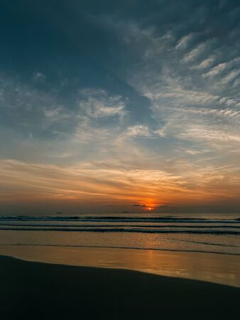 Dawn on the sea with a view of the horizon, colorful sky from the sun rays, clouds on a blue sky. Sandy beach on the seashore, waves on the sea, copy placeの写真素材
