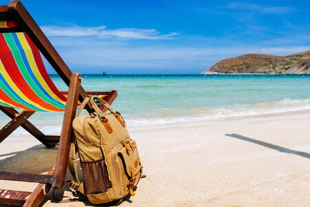 A place for the traveler, freelancer. A deck chair on the sandy shore of a tropical beach overlooking the open sea. a stylish brown backpack standing nearby. The concept of remote work, recreationの写真素材