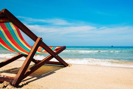 Deck chair on the sandy beach by the sea. The bruise color of the water and the blue sky with broken clouds in the background. A place for relaxation and freelance work. Open sea view with boats on the horizonの写真素材