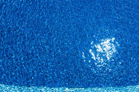 Swimming pool, blue clear water in the outdoor pool, with sun flare on the surface. Background of blue water in the pool. Ripples on the surface of the water. Copy placeの写真素材