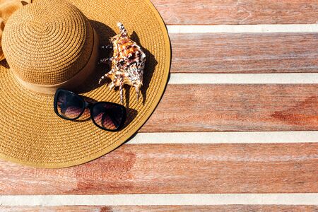 female straw hat on a wooden background with seashells. The concept of vacation and sea vacation. Copy place. Space for text or insertion. Beach accessories.の写真素材