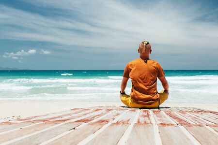 guy sits on the shore of a tropical beach The view from the back, the place of meditation, relaxation, during summer vacation. A panoramic view of the sea with a sandy beach, clear summer day. Copy placeの写真素材