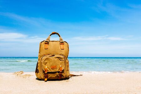 vacation, freedom. Empty tropical landscape with a sandy beach by the sea. A traveler's backpack on the shore. Blue sky with white clouds and bruise sea in the background. Place to paste, copy placeの写真素材