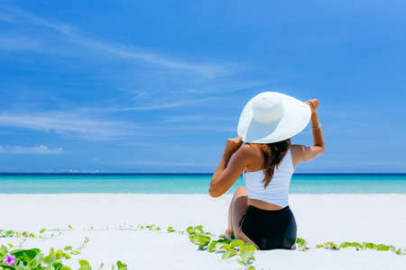 A young pretty girl lies on the white sand by the ocean with bruise water. A paradise for travel on vacation. Looks towards the sea, enjoyment in a beautiful place. copy place.の写真素材