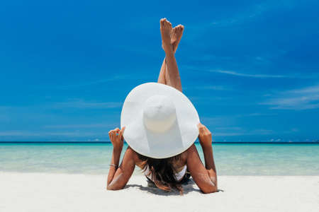 A young pretty girl lies on the white sand by the ocean with bruise water. A paradise for travel on vacation. Looks towards the sea, enjoyment in a beautiful place. copy place.の写真素材