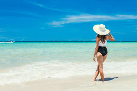 A young pretty girl lies on the white sand by the ocean with bruise water. A paradise for travel on vacation. Looks towards the sea, enjoyment in a beautiful place. copy place.の写真素材