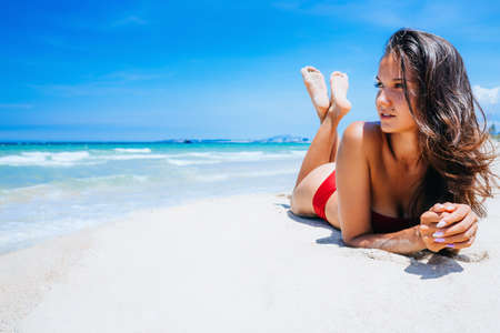 A young pretty girl lies on the white sand by the ocean with bruise water. A paradise for travel on vacation. Looks towards the sea, enjoyment in a beautiful place. copy place.の写真素材