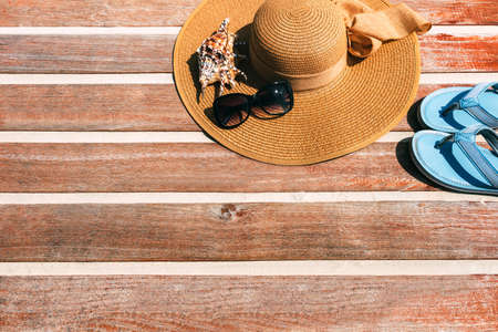 concept of vacation. Top view of a female straw hat on a wooden background with seashells and slippers. Copy place. Space for text or insertion. Beach accessories.の写真素材