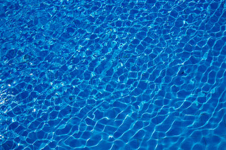 Swimming pool, blue clear water in the outdoor pool, with sun flare on the surface. Background of blue water in the pool. Ripples on the surface of the water. Copy placeの写真素材