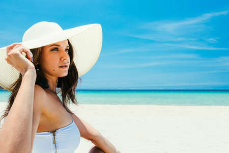 Portrait of a young girl in a straw hat on a tropical beach with white sand and turquoise water in the sea. A triple paradise for relaxation. copy spaceの写真素材