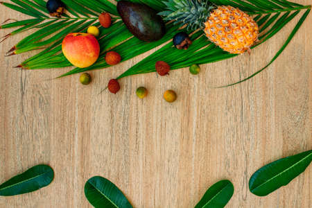 Flat lay Mix of Exotic fruits and palm leaf on a brown background: pineapples, Avocado, mangoes, mangosteen, lychee, citrus fruits. A great set for a healthy diet. Vegetarianism with fruits. Copy space, wood backgroundの写真素材